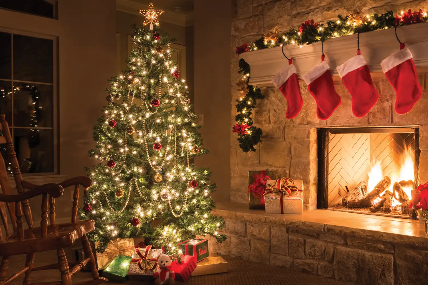 A brightly-lit and dressed Christmas tree in a lounge, in front of a roaring open fire on Christmas Eve. Stockings hang above the fireplace